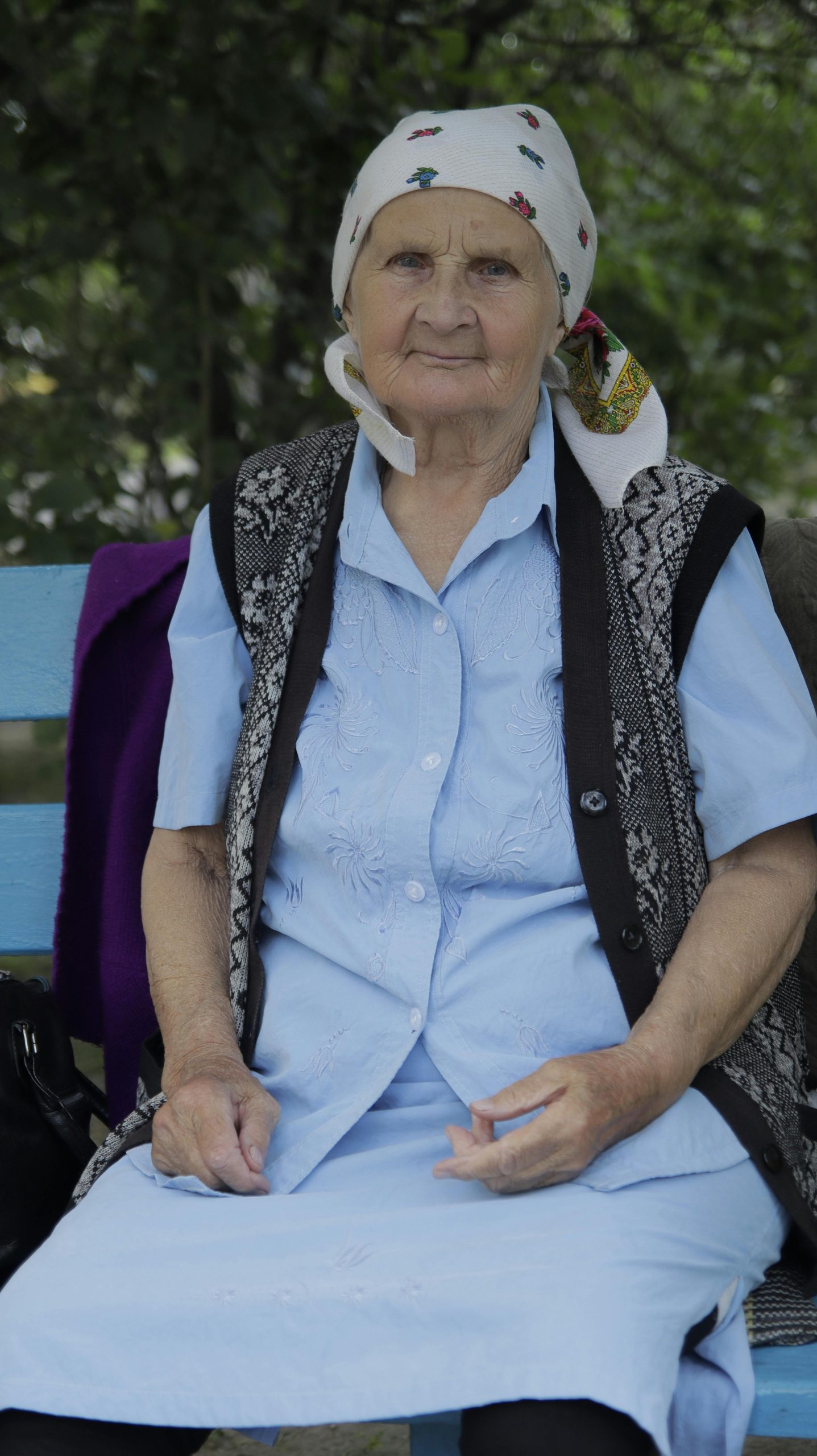Senior woman in headscarf sitting on a bench outdoors, looking thoughtfully.