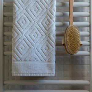 Elegant white towel with geometric pattern on bathroom towel rail, paired with a natural bristle brush.