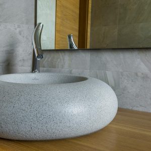 Elegant stone bathroom sink with modern chrome faucet and large mirror.